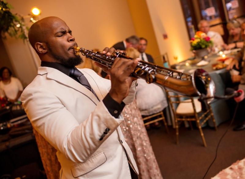 A close-up shot of a musician playing a saxophone for a couple during a wedding celebration in the spacious MSU Riley Center Exhibit Hall.